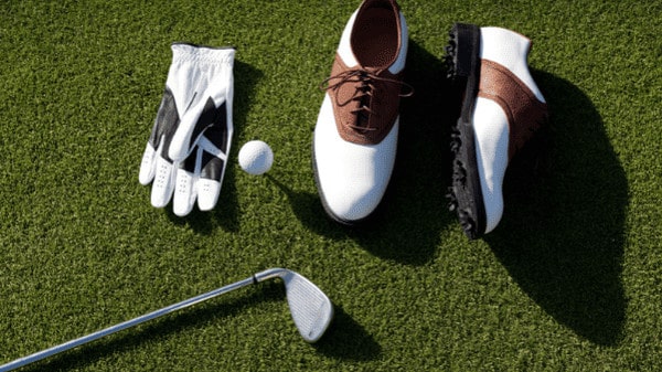 a pair of white and brown shoes next to a golf club