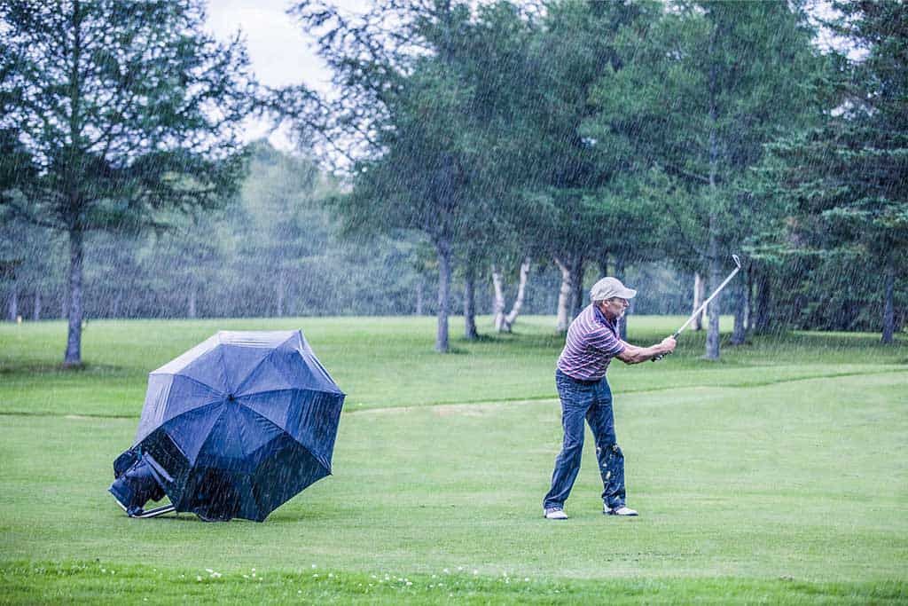 6 Tips for Golfing in the Wind and a man playing golf in bad weather.