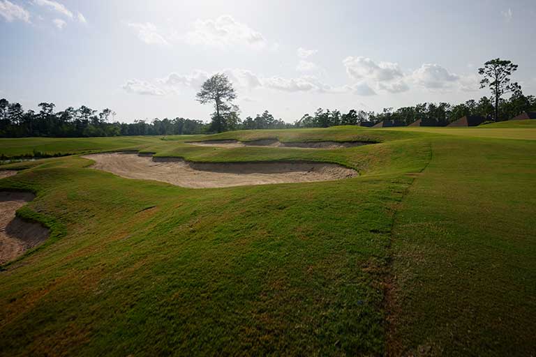 a golf course with sand bunkers and trees in the background