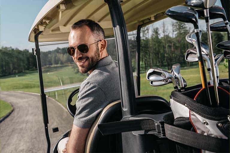Man with sunglasses smiling in a golf cart with clubs in the back.