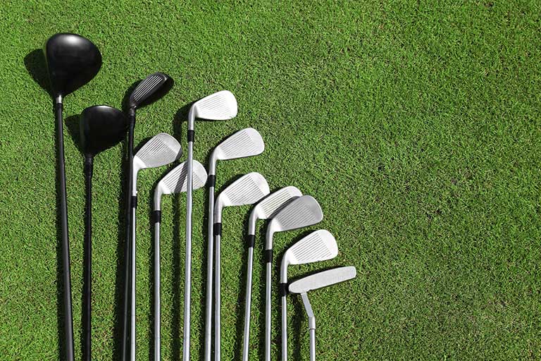 A variety of golf clubs aligned on green grass, including drivers and irons. This is about how to clean your golf clubs, grips and shoes