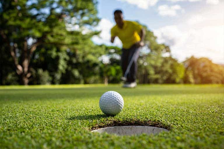 A man is practicing his short game by sinking a golf ball into a hole.