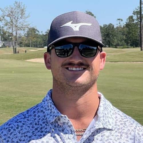 a man wearing sunglasses and a hat standing in front of a golf course