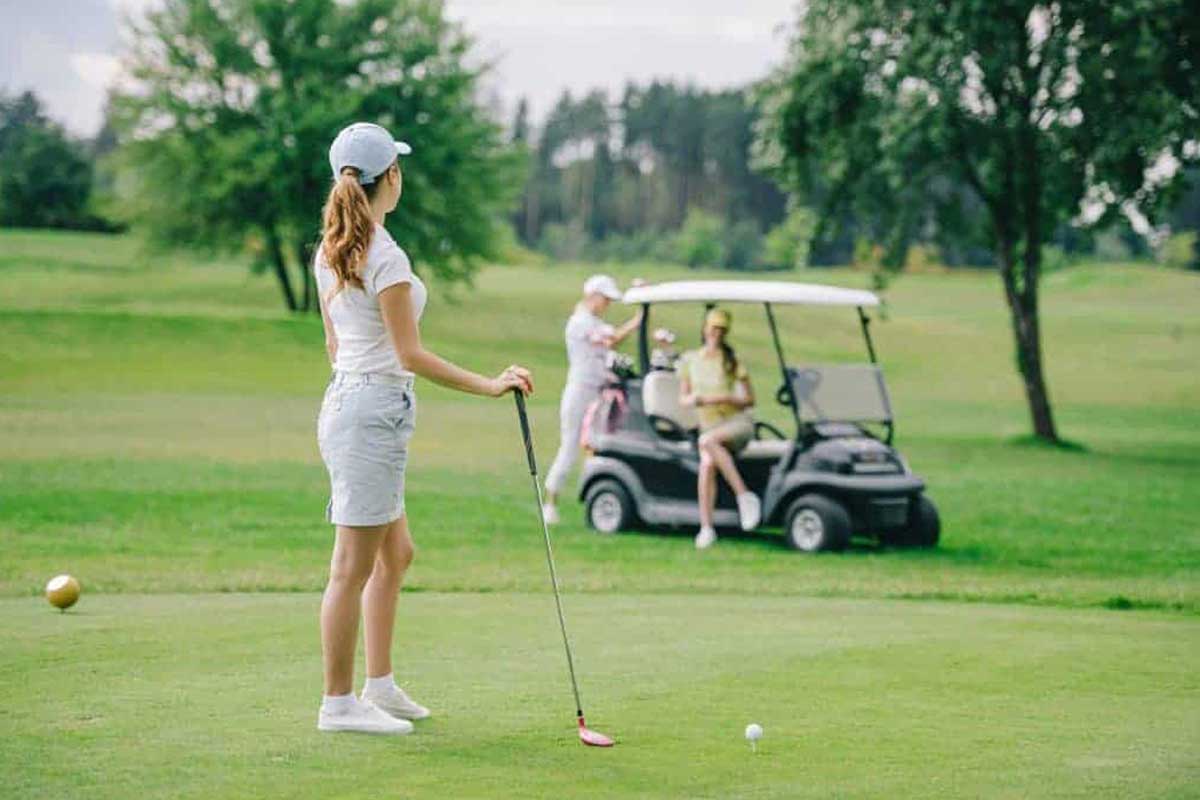A woman is practicing golf drills to improve her game on the course while utilizing a golf cart.